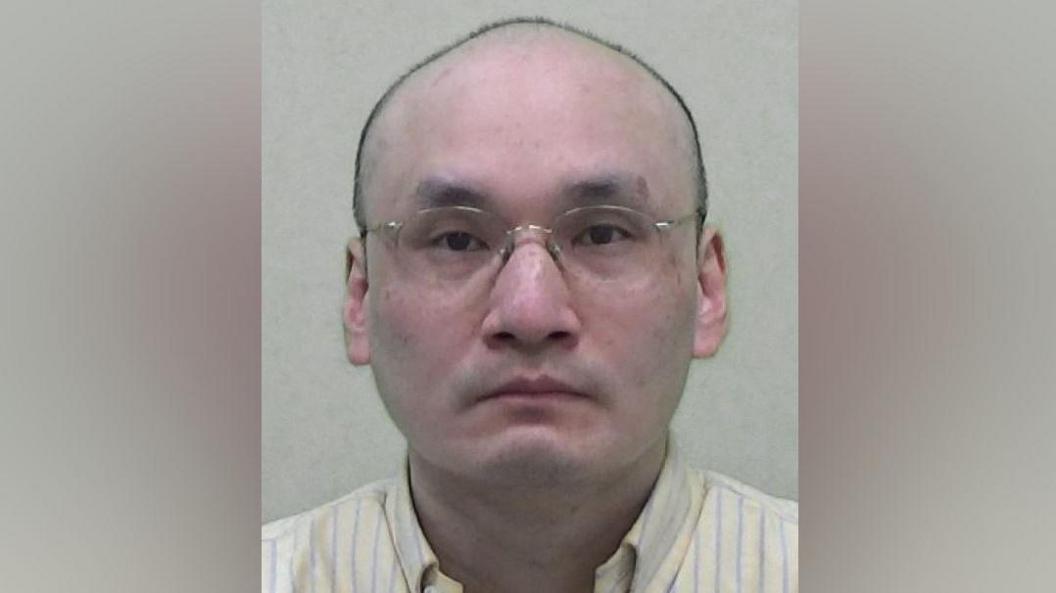 Mugshot of Thomas Kwan. He is bald and clean shaven with thin framed glasses.