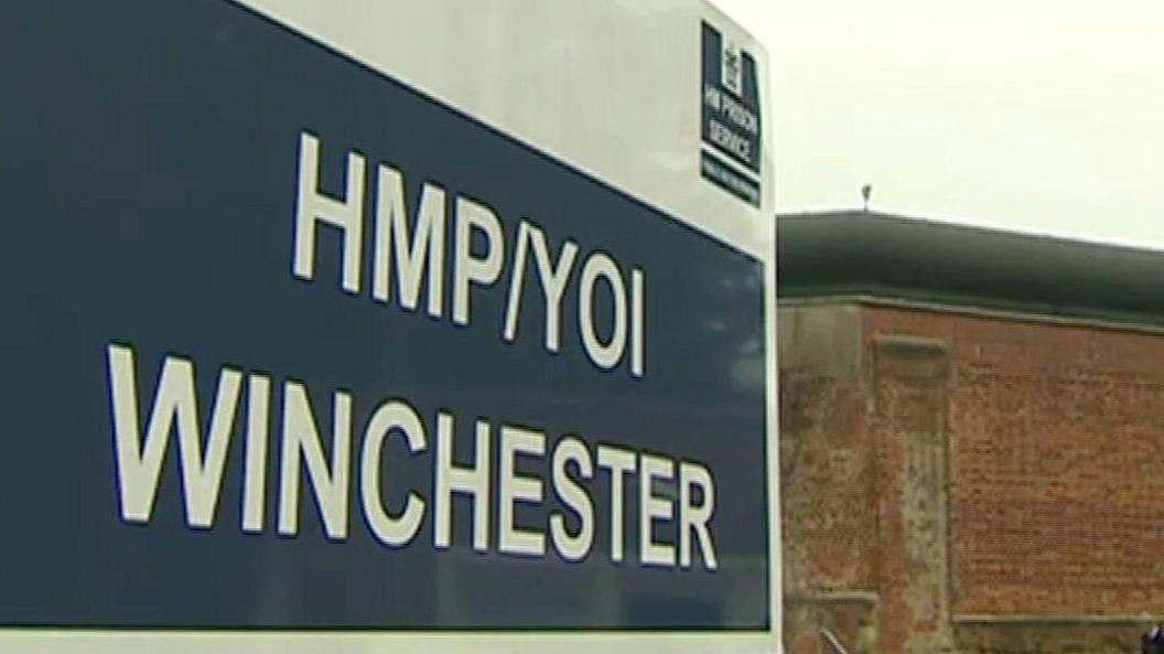 Exterior photograph of HMP Winchester with the sign in the foreground and prison walls in the background