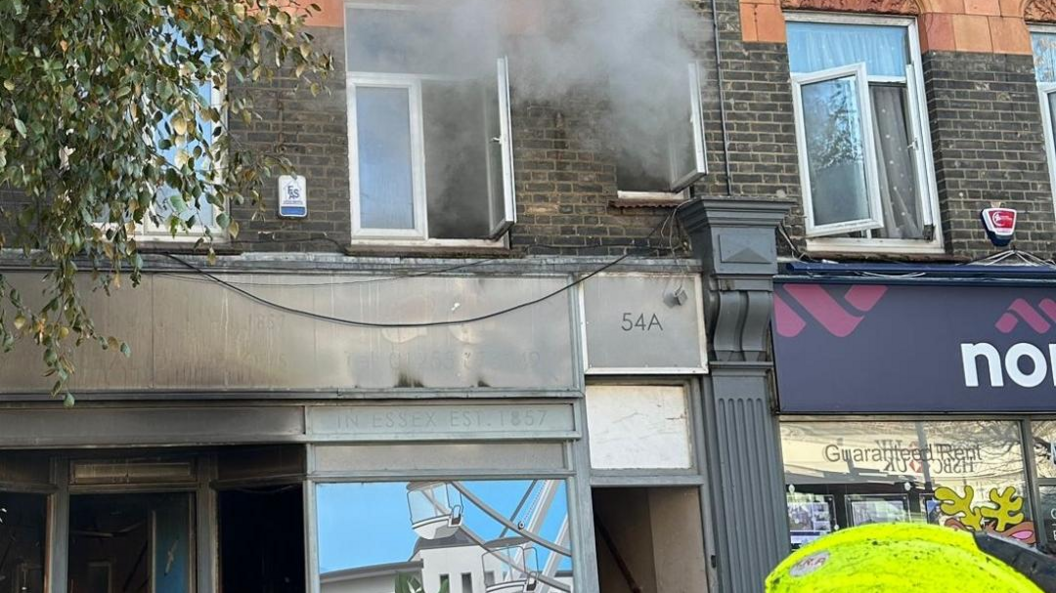 Burnt out shop front with smoke coming from two upper storey windows.