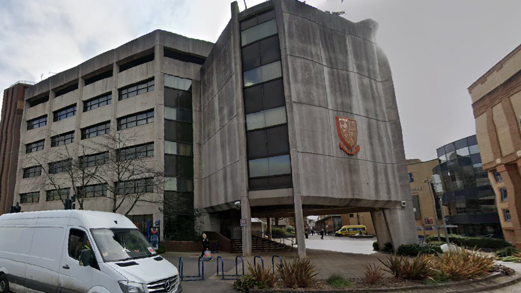 A grey concrete building with a red crest on the side of it.