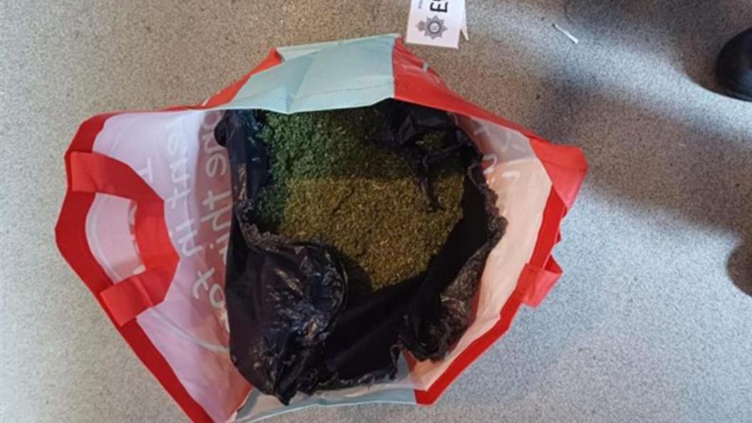 A red and while bag for life containing a plant-like substance.