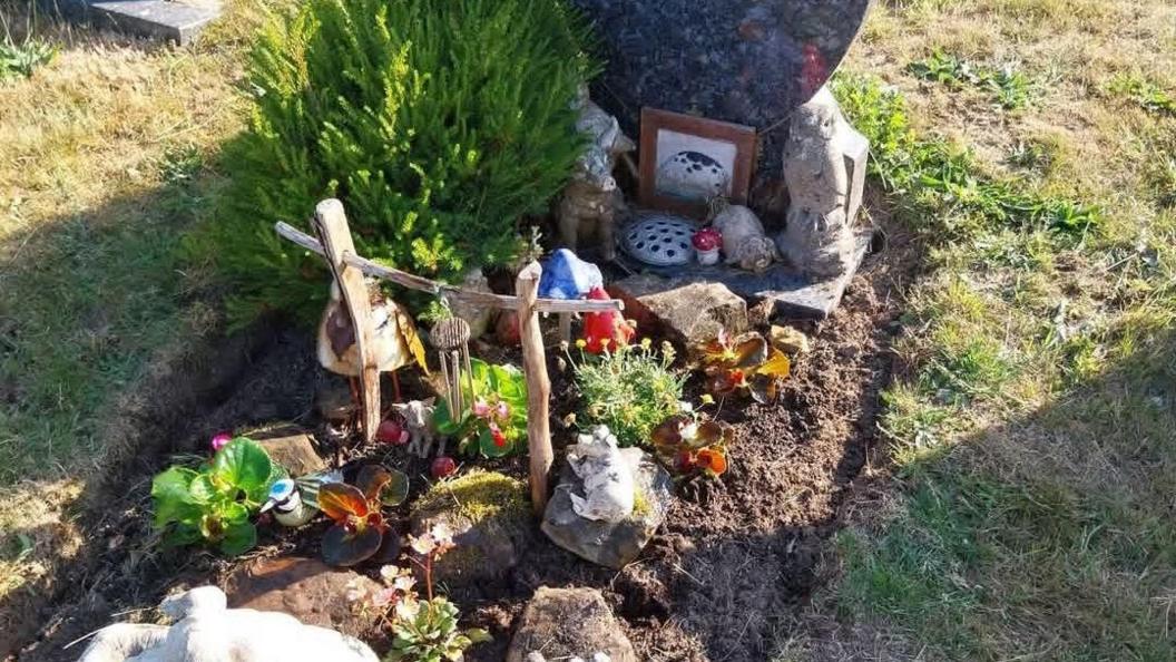 A grave covered in several mementos, including windchimes and statues.