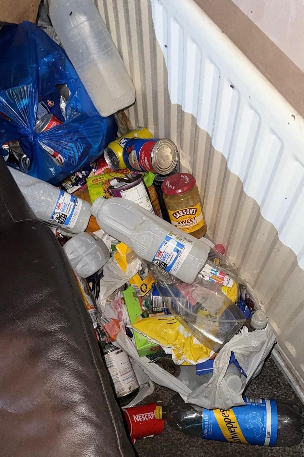 Empty plastic milk bottles, glass jars and tins piled up next to a radiator.