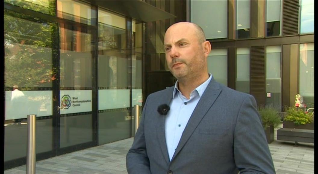 Matt Golby, wearing a charcoal blazer and blue shirt, stands in front of the council offices. 