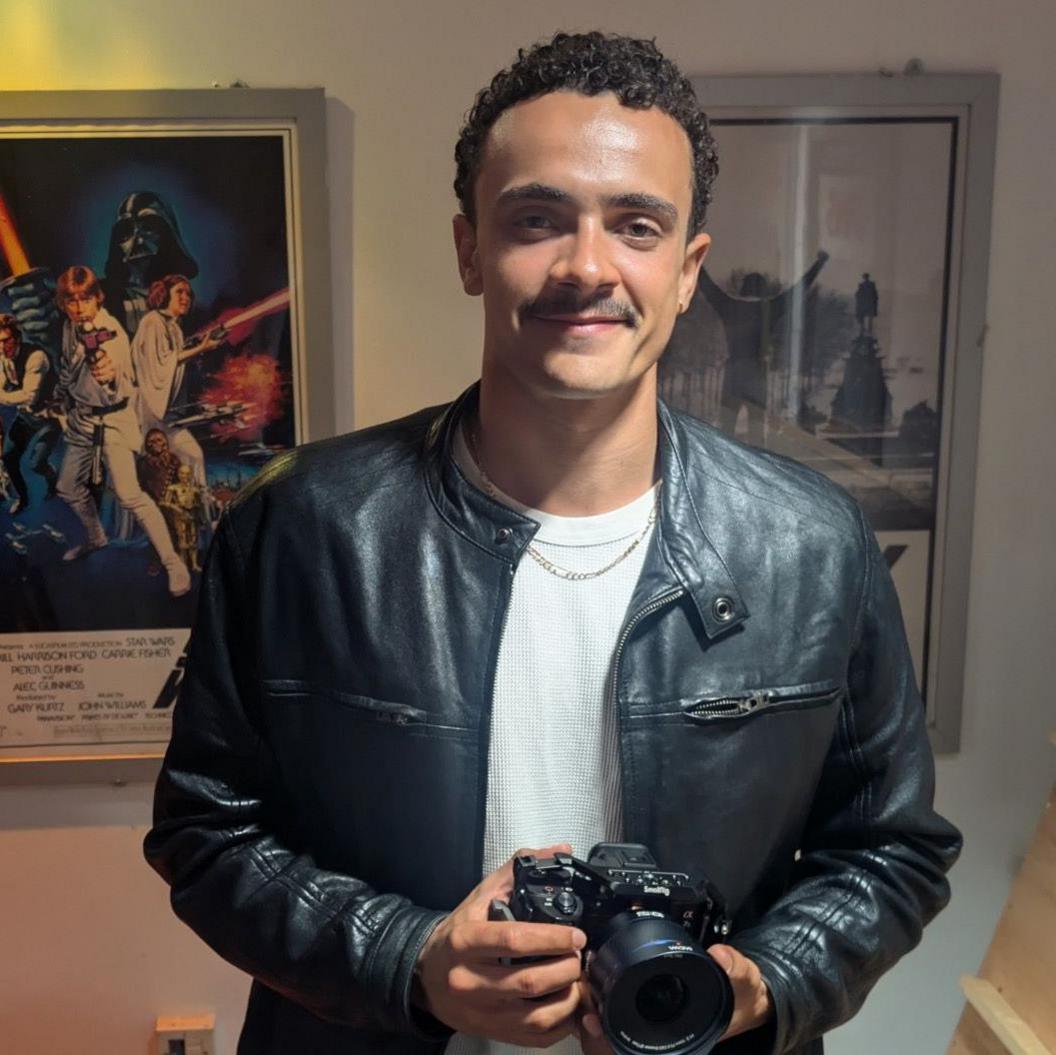 Filmmaker Sebastian Piette Pereira wearing a white T-shirt and black leather jacket against a background of classic film posters including Rocky and Star Wars