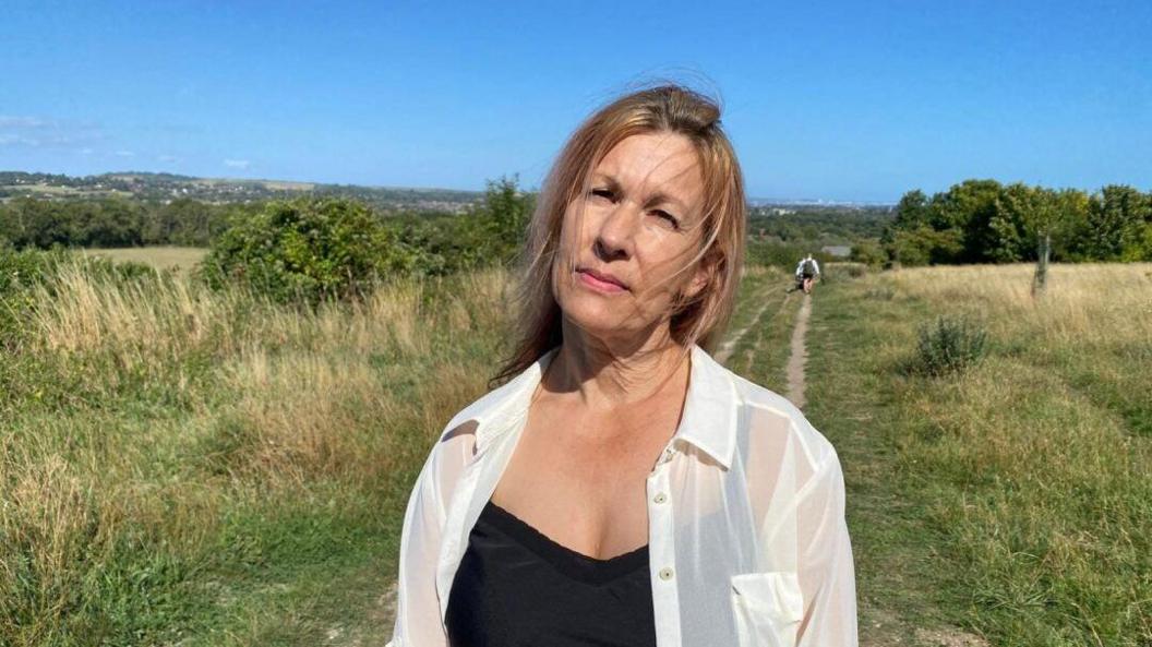 A woman in the white top. She is standing in a field on a summer's day.