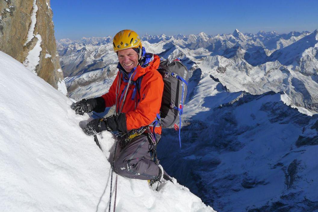 Mick Fowler, in an orange jacket and with a yellow helmet, climbing a mountain