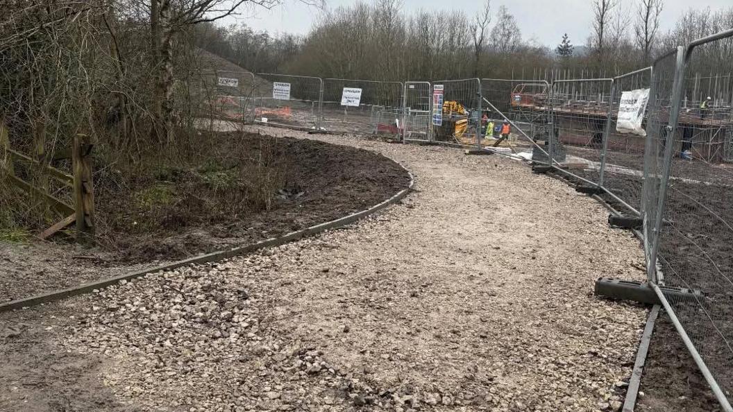 A gravelled path winding past the boundary of a construction site