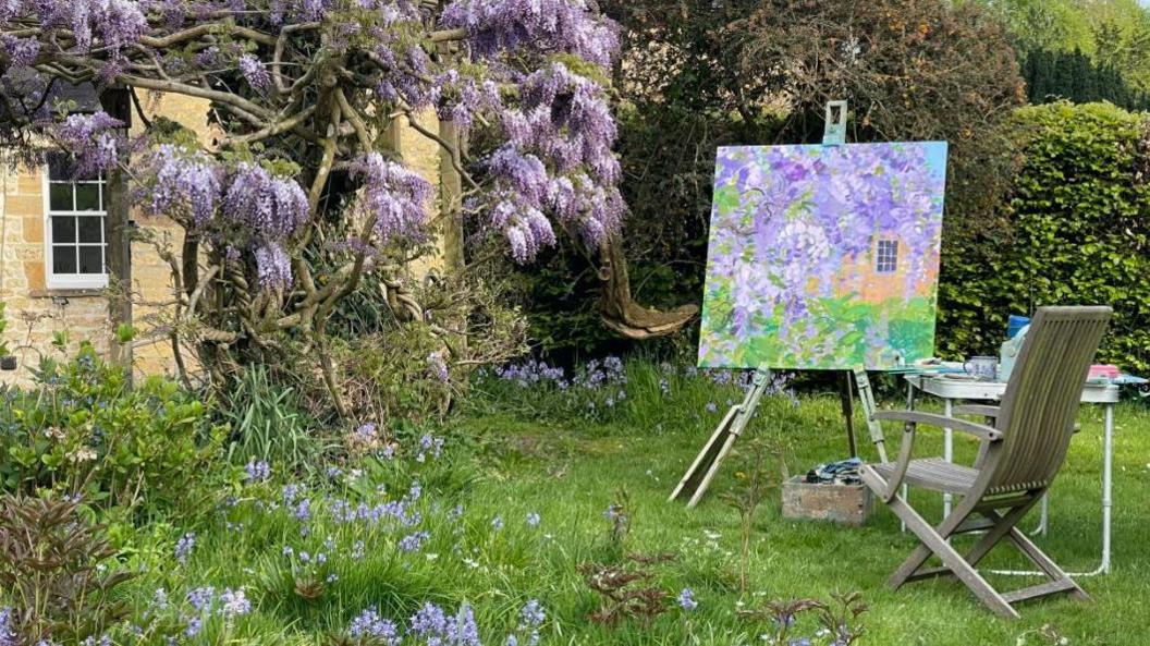 A painting of a wisteria tree, which has purple petals. the painting is being completed outside in a garden facing the wisteria.
