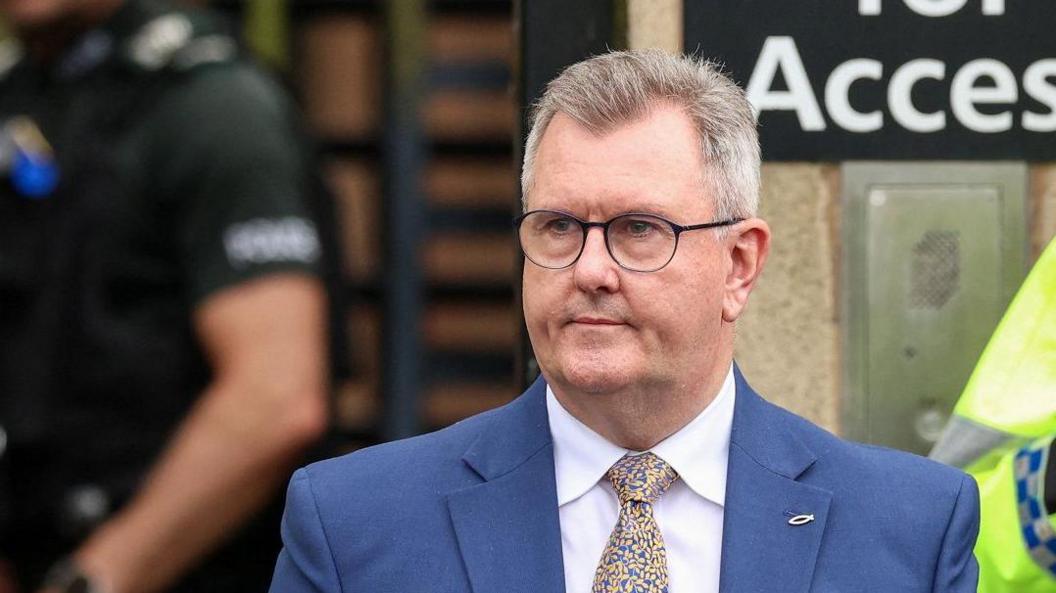 Jeffrey Donaldson is pictured looking off to the side of the camera. He is dressed in a blue suit and white shirt with a patterned tie. 