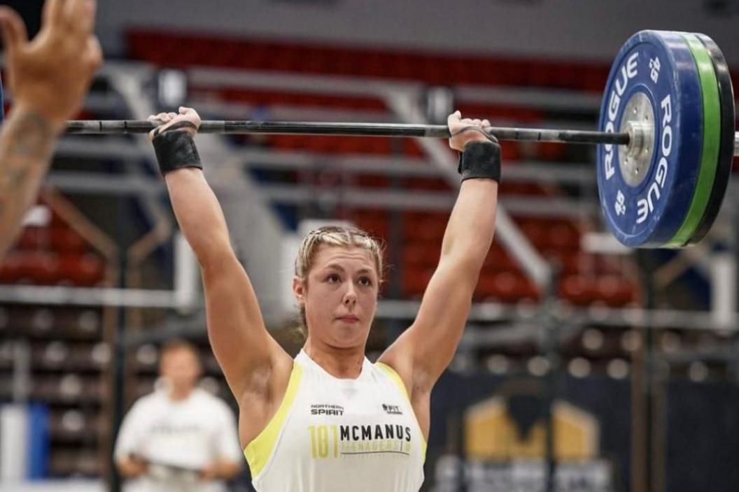 A girl in a white vest holding a weightlifting bar above her head