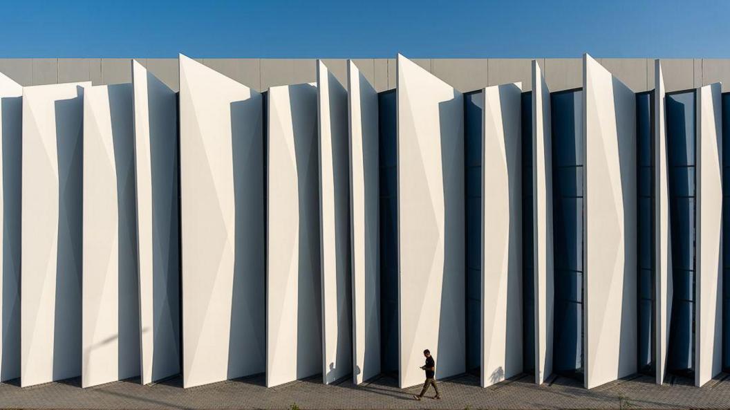 The exterior of a Khazna data centre in Masdar City, Abu Dhabi - it is white and has a "concertina" appearance. The small figure of a man in a suit is walking in front of it.