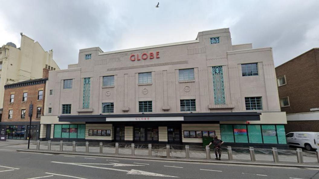 The Stockton Globe. The grey stone building has been made in the art deco style. The word Globe stands in red letters at the top of the building. Green metalwork decorates the building.