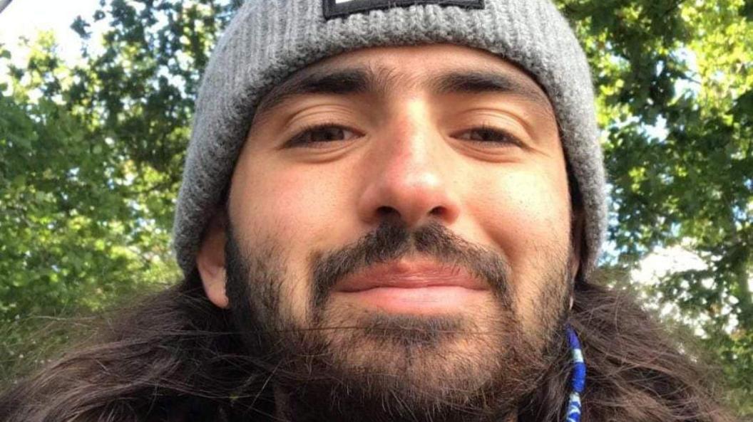 A selfie of Michael. He is wearing a grey knitted hat and is pictured outside underneath some trees.