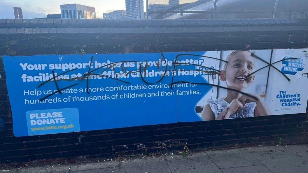 A billboard for the Sheffield Children's Hospital Charity which reads: "Yours support helps us provide better facilities at the hospital." However, a graffiti tag has been sprayed across the entire sign, including a photo of a little girl using a breathing tube.