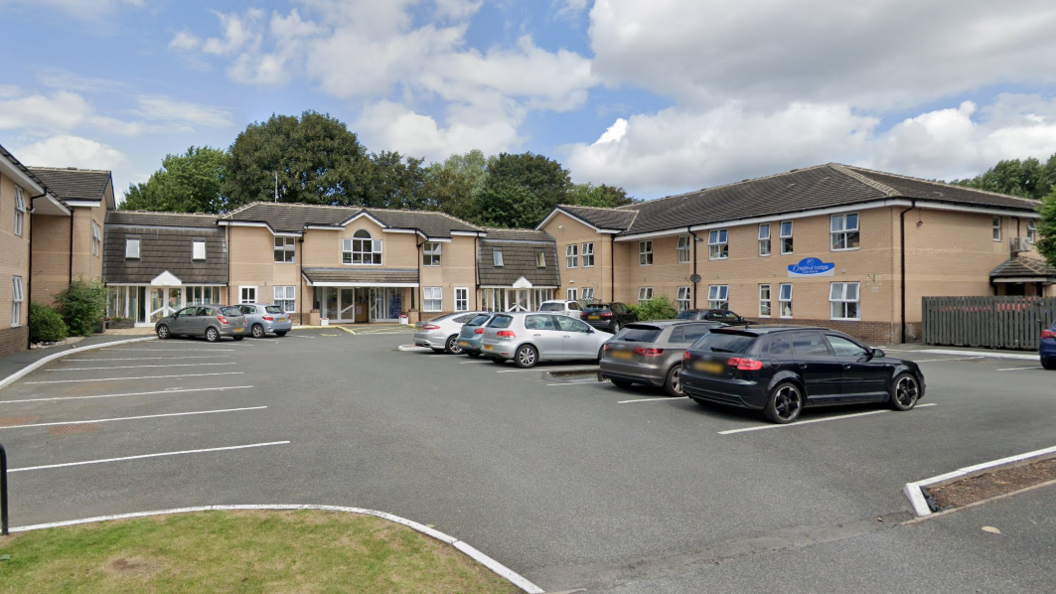 A car park with several cars in front of a large two-storey building.