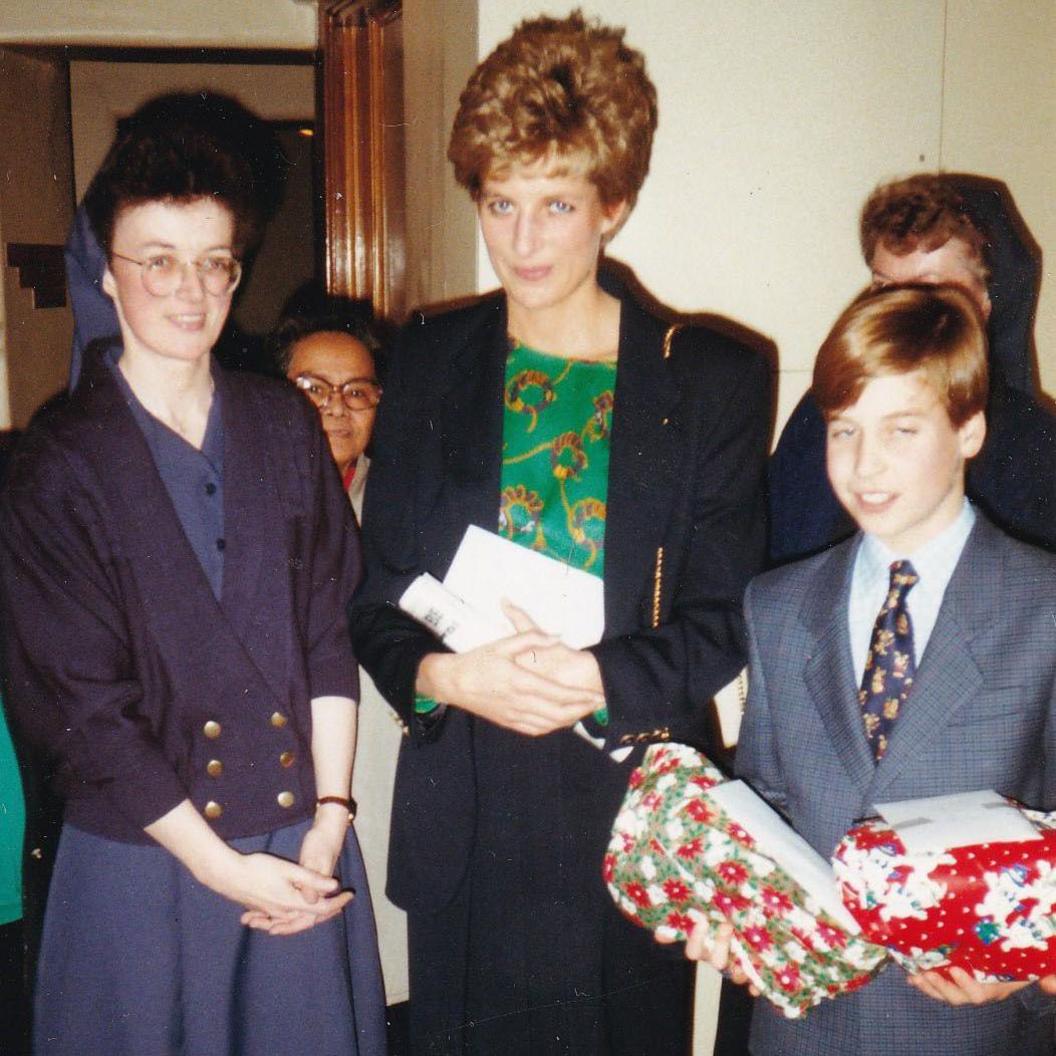 Prince William, standing to the left of his mother Diana holding two red wrapped presents while wearing a suit in 1993