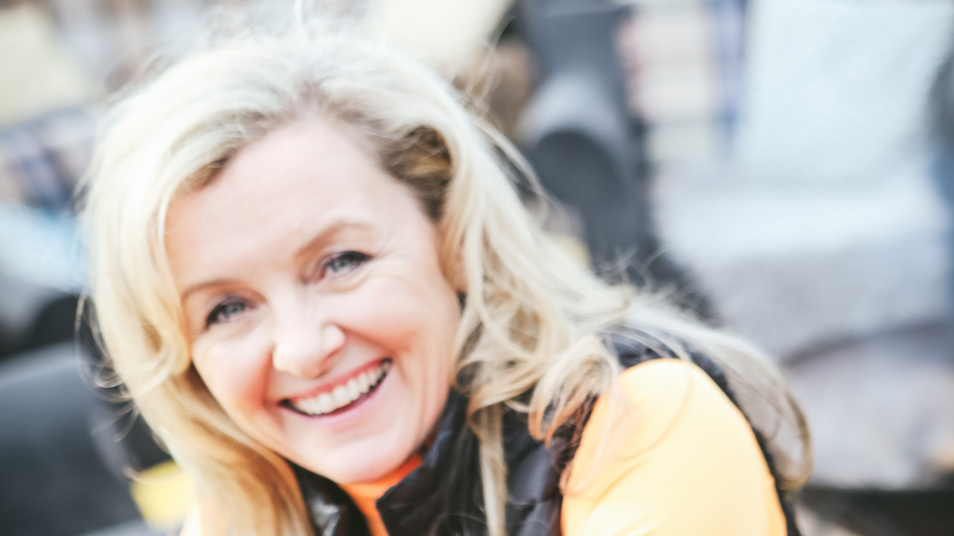 Ruth Astbury looking at the camera. She has blonde hair and an orange top paired with a gilet.