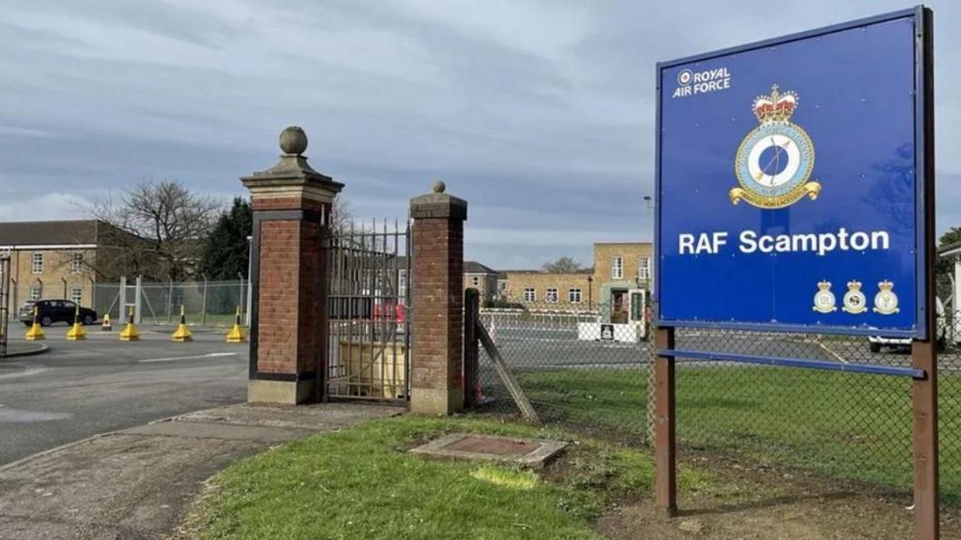 A large blue sign stating "RAF Scampton and the Royal Air Force badge at the entrance to RAF Scampton