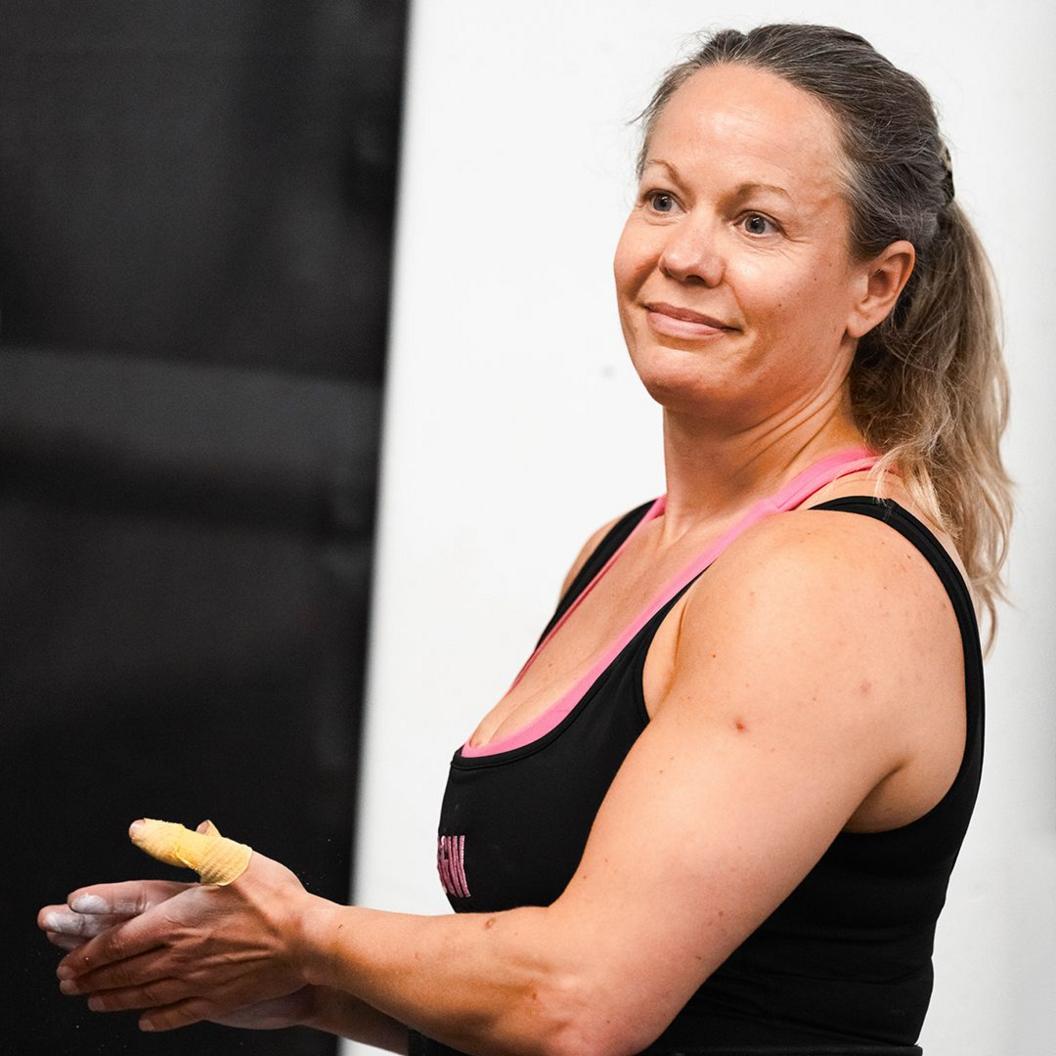 Ali Watson at the gym, smiling at the camera and rubbing chalk on her hands 
