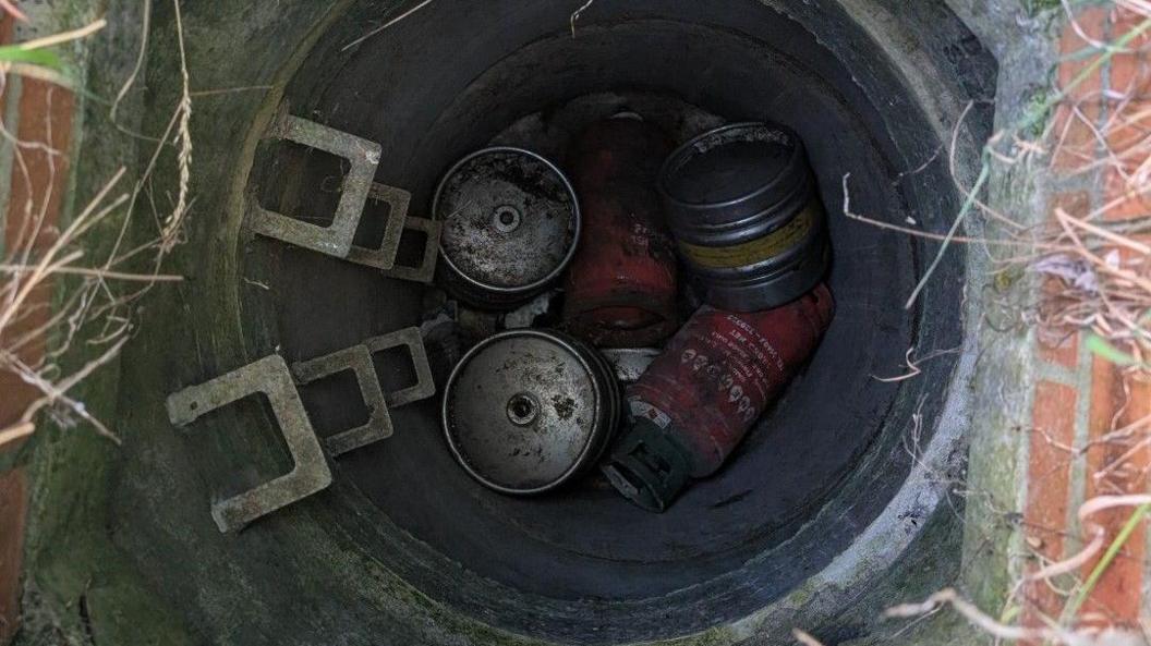 A picture of a well, showing metal steps down to it, several cylinders in it,
