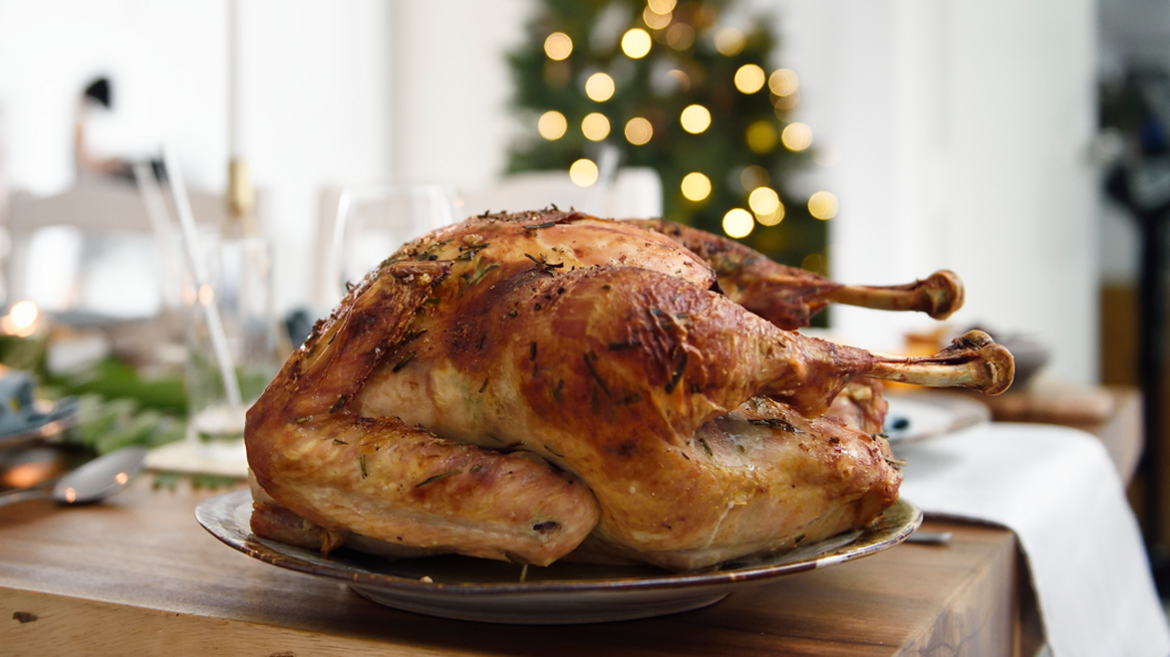 A roast turkey on a silver plate on a table, with a blurry shape of a christmas tree in the background