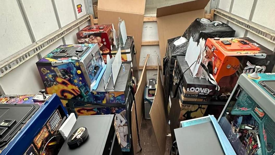 Six pinball machines in a container with cardboard on top of them, ready for transportation to the hotel. 