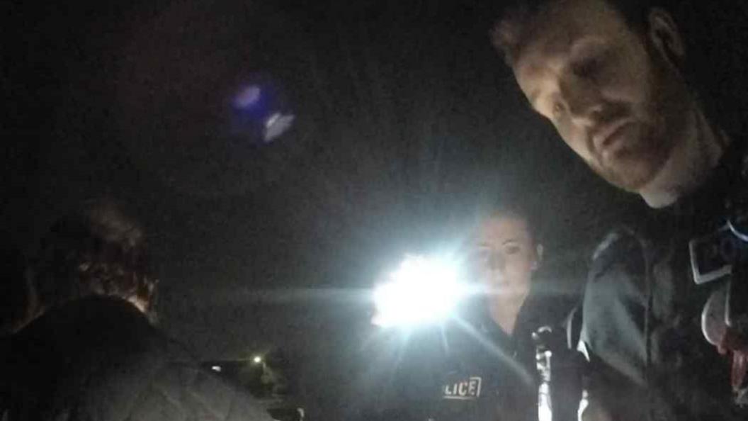 Picture of two police officers, on of which is holding a torch. You can also see the back of a mans head. 