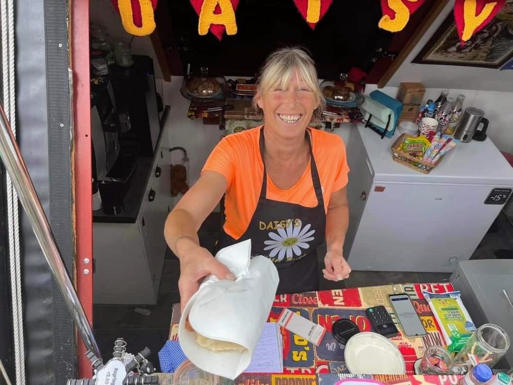 Daisy Hampshire in an orange t-shirt and black apron with a daisy on, in a canal boat handing a sandwich over with a smile