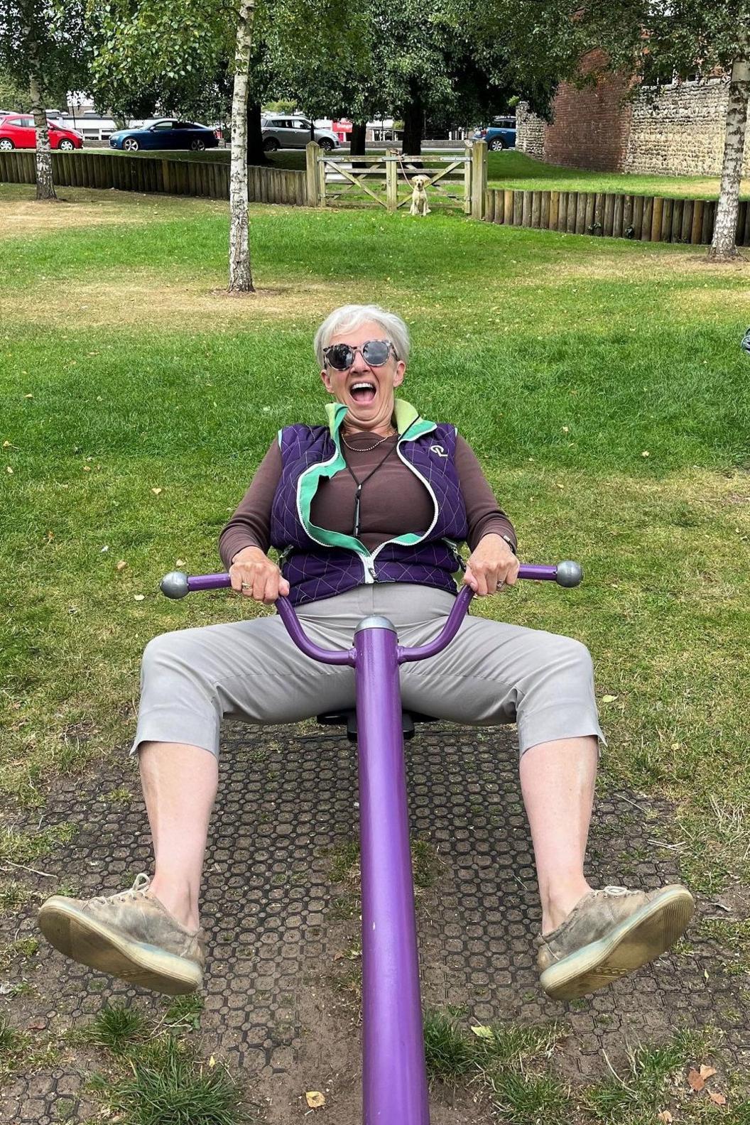 Woman smiling sitting on a seesaw and holding on to the handles