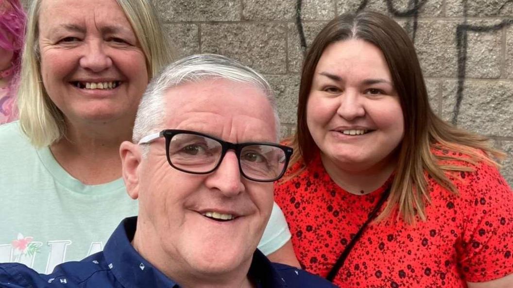 One man wearing dark-rimmed glasses and two women, one with blonde hair and Amy, with dark hair