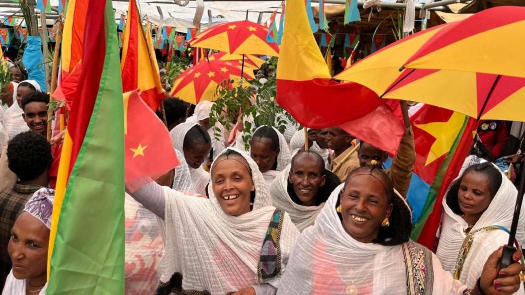 Smiling women way flags and umbrellas with the Eritrean and Tigrayan colours.