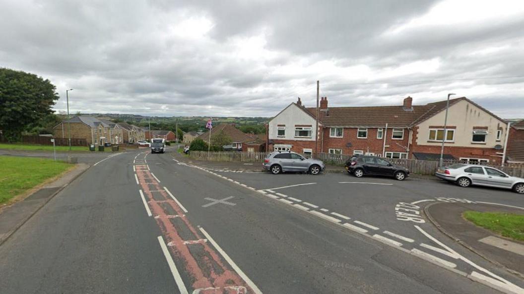 A junction where three cars are parked closely to the turning. There is a car approaching the junction. 