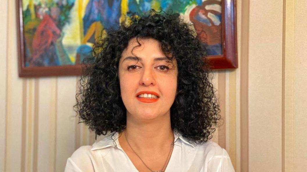 A headshot of Narges Mohammadi  - she looks towards the camera and smiles while wearing a white blouse.