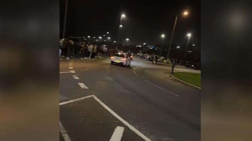 A still from a video of a white car spinning out of control towards a crowd of people