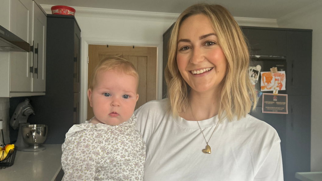 Bethan mewn crys-t Gwyn yn dal ei babi Nel