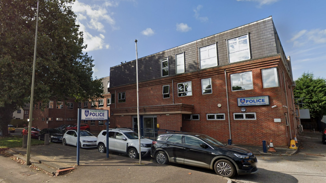 A general view picture of Banbury police station, a three-storey building with a row of cars parked outside its entrance.