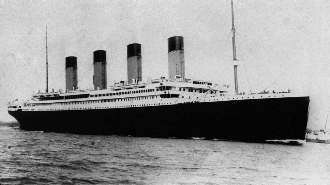 Black and white photo from about 1912 of the four-funnelled ship on water. it has balck hull and white cabins above.