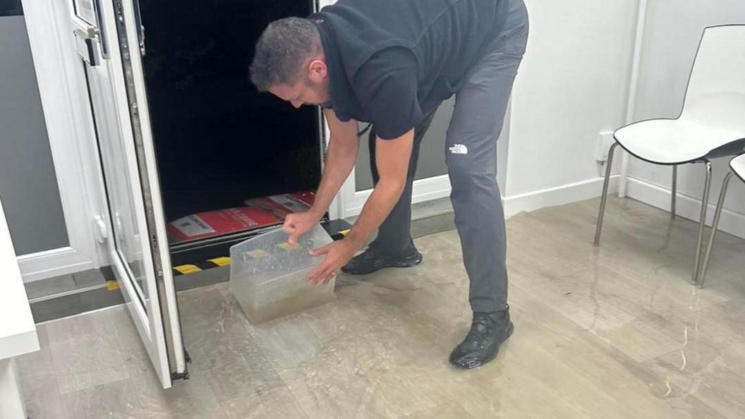 A man with a container scooping water out of a business premises