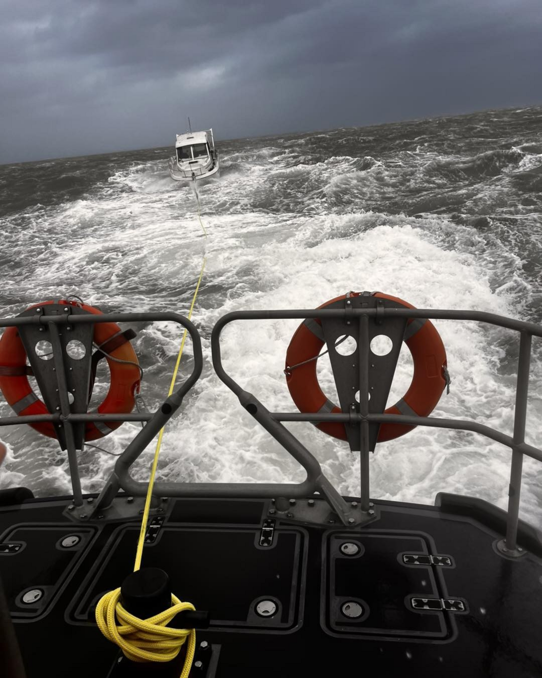 A small white boat being towed using a long yellow rope by a lifeboat.