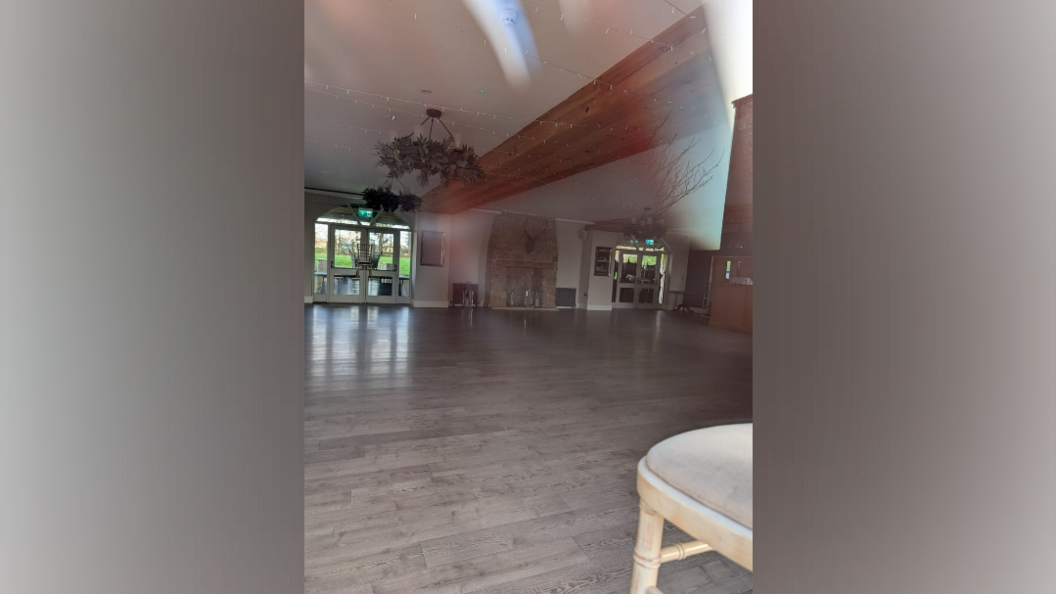 A large empty hall with a light grey floor. A wooden beam stretches across the ceiling.