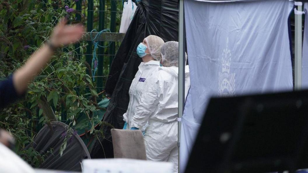 Two people in white hazmat suits looking at a fence