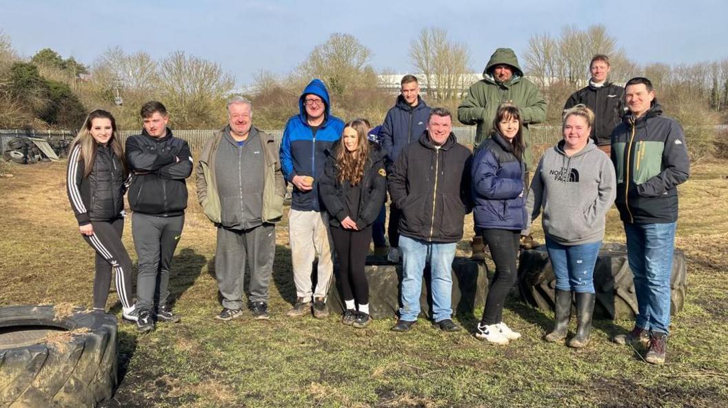 A group of people standing in a field near large industrial tyres