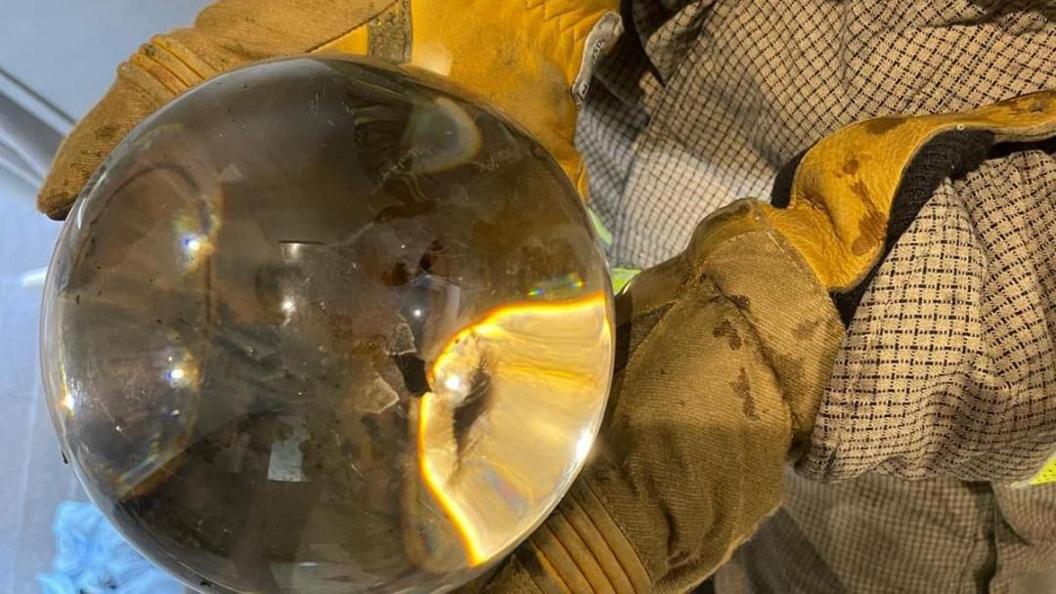 A decorative globe being held by a person wearing yellow gloves. It has minor fire damage.