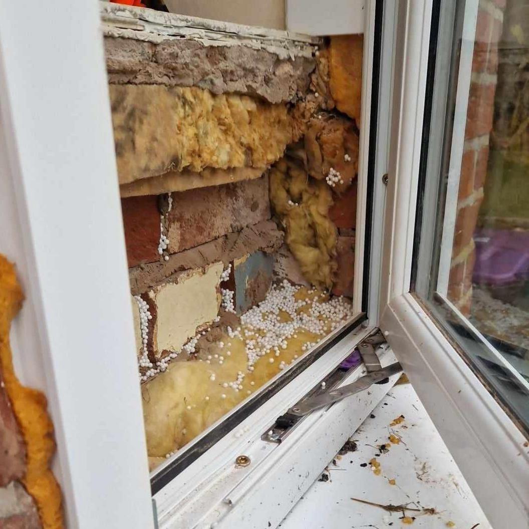 A white PVC window unit with untidy brickwork behind and insulation poking through 