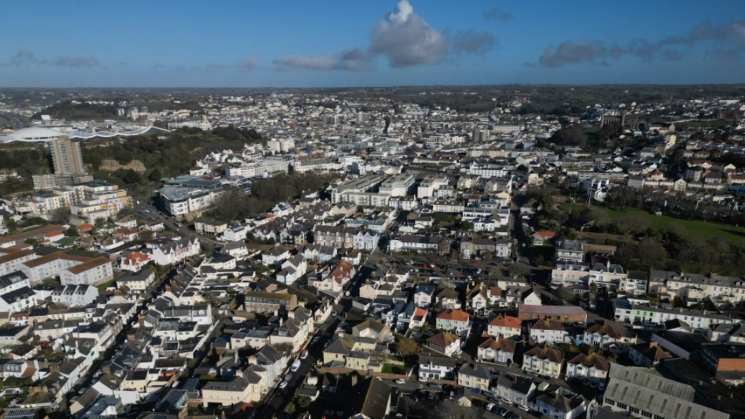 Ariel shot of South St Helier. Jersey. There are rows of houses and buildings below. The photo was taken on a cloudy day.