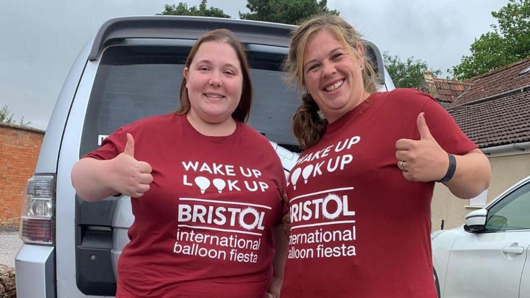 Mandy Thompson and her friend Katie giving a thumbs up to the camera. They are both smiling and wearing red T-shirts