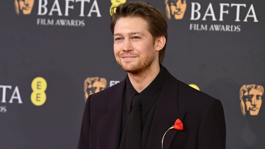 Joe Alwyn with a single red flower on his dark suit