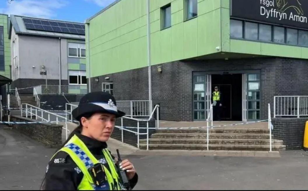 Police officer stood outside Ysgol Dyffryn Aman with police tape across the steps behind her