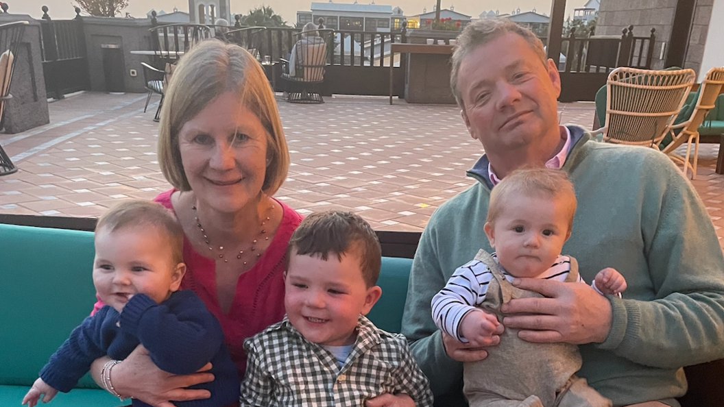 A woman with blonde hair and a red dress, along with a fair-haired man in a green jumper sit with three toddlers on their knees.